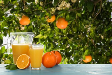 Image of Fresh orange juice on light blue wooden table in orchard. Space for text