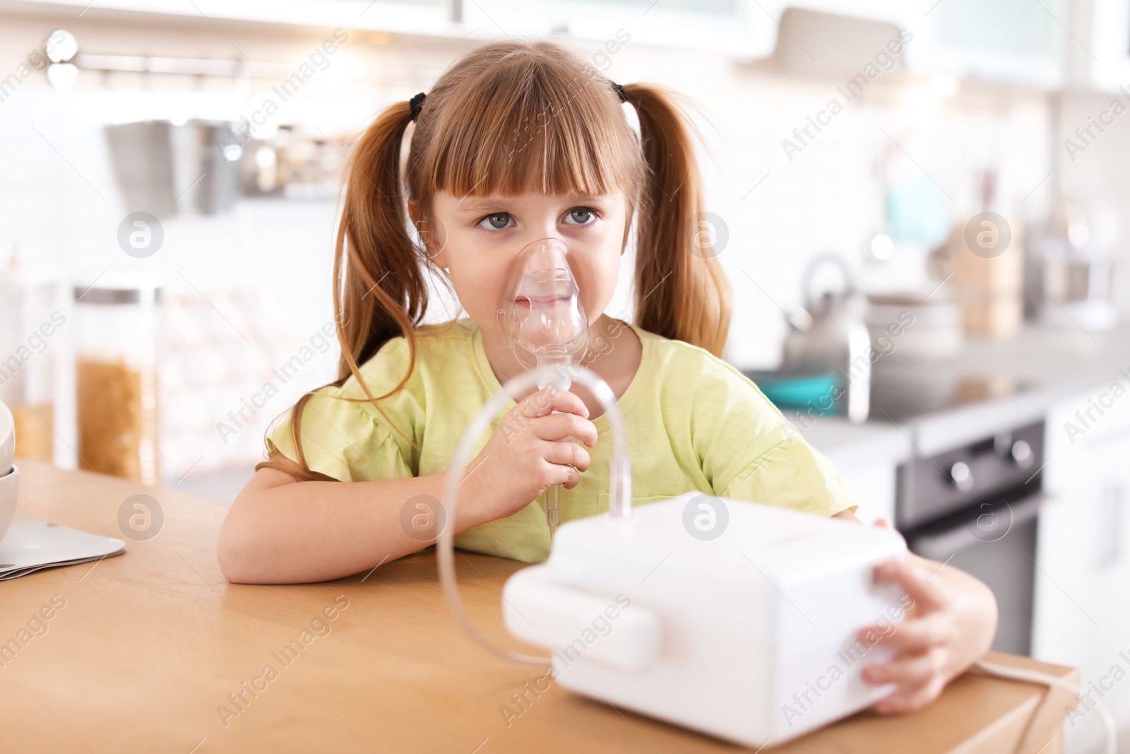 Photo of Little girl using asthma machine at table in kitchen