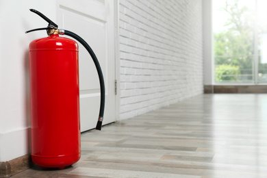 Photo of Fire extinguisher on floor near door indoors, space for text
