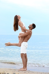 Young man holding his girlfriend in bikini on beach. Lovely couple