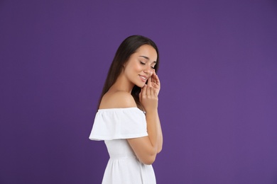 Young woman wearing stylish white dress on purple background