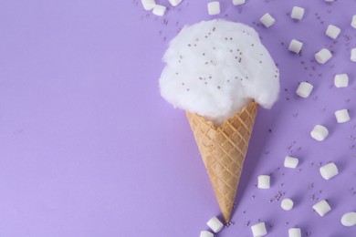 Photo of Sweet cotton candy in waffle cone and marshmallows on purple background, flat lay. Space for text