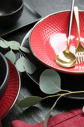 Stylish ceramic plates, cutlery and floral decor on grey table, closeup