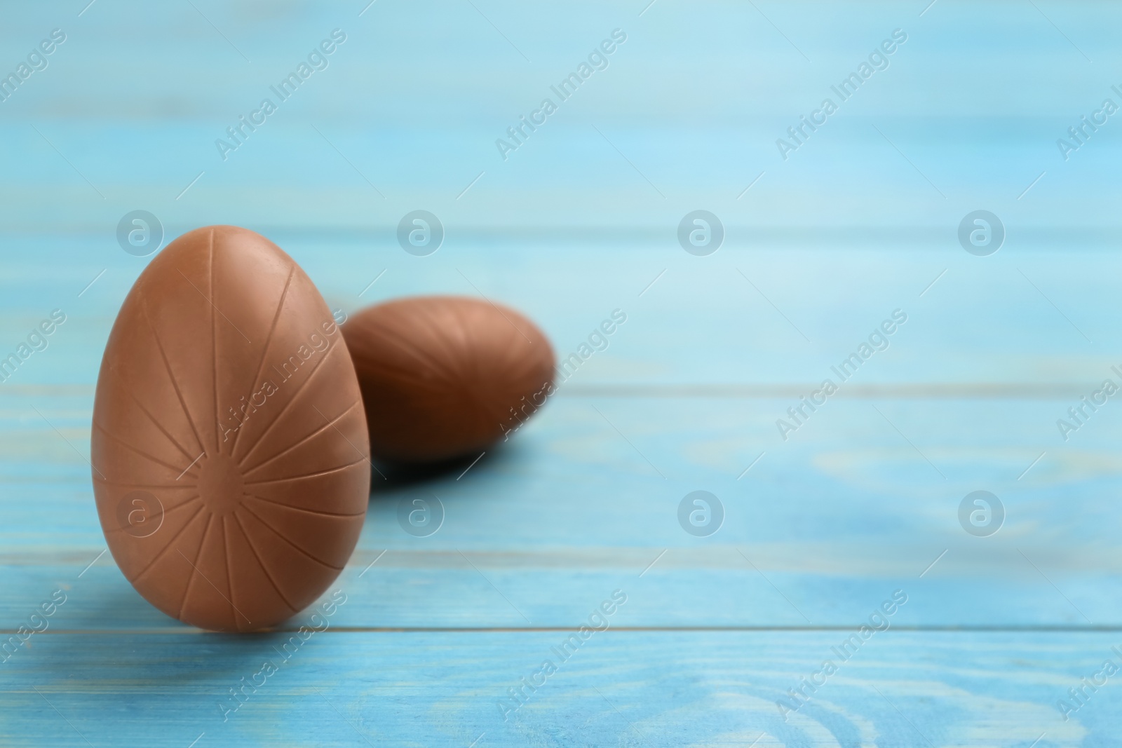 Photo of Sweet chocolate eggs on light blue wooden table. Space for text