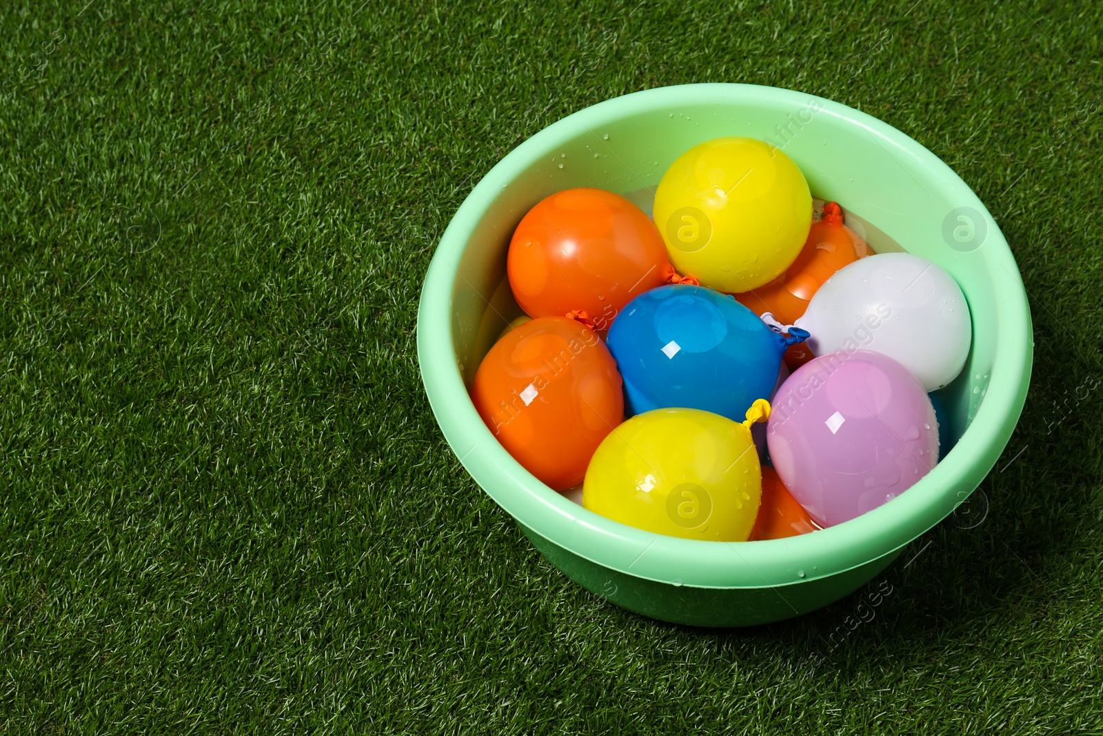 Photo of Basin full of colorful water bombs on green grass. Space for text