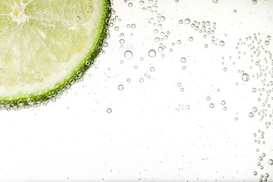 Photo of Juicy lime slice in soda water against white background, closeup. Space for text