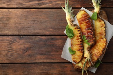 Tasty grilled pineapple pieces and mint leaves on wooden table, top view. Space for text