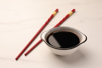 Bowl with soy sauce and chopsticks on white marble table