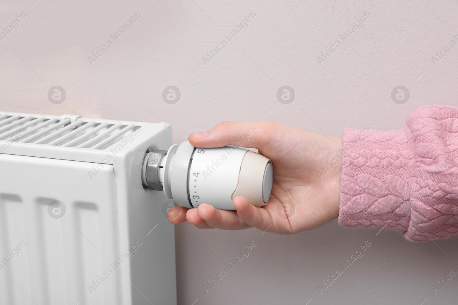 Photo of Girl adjusting heating radiator thermostat near white wall indoors, closeup