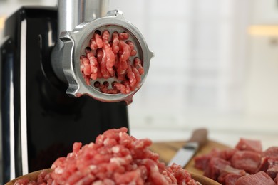 Electric meat grinder with beef on blurred background, closeup. Space for text