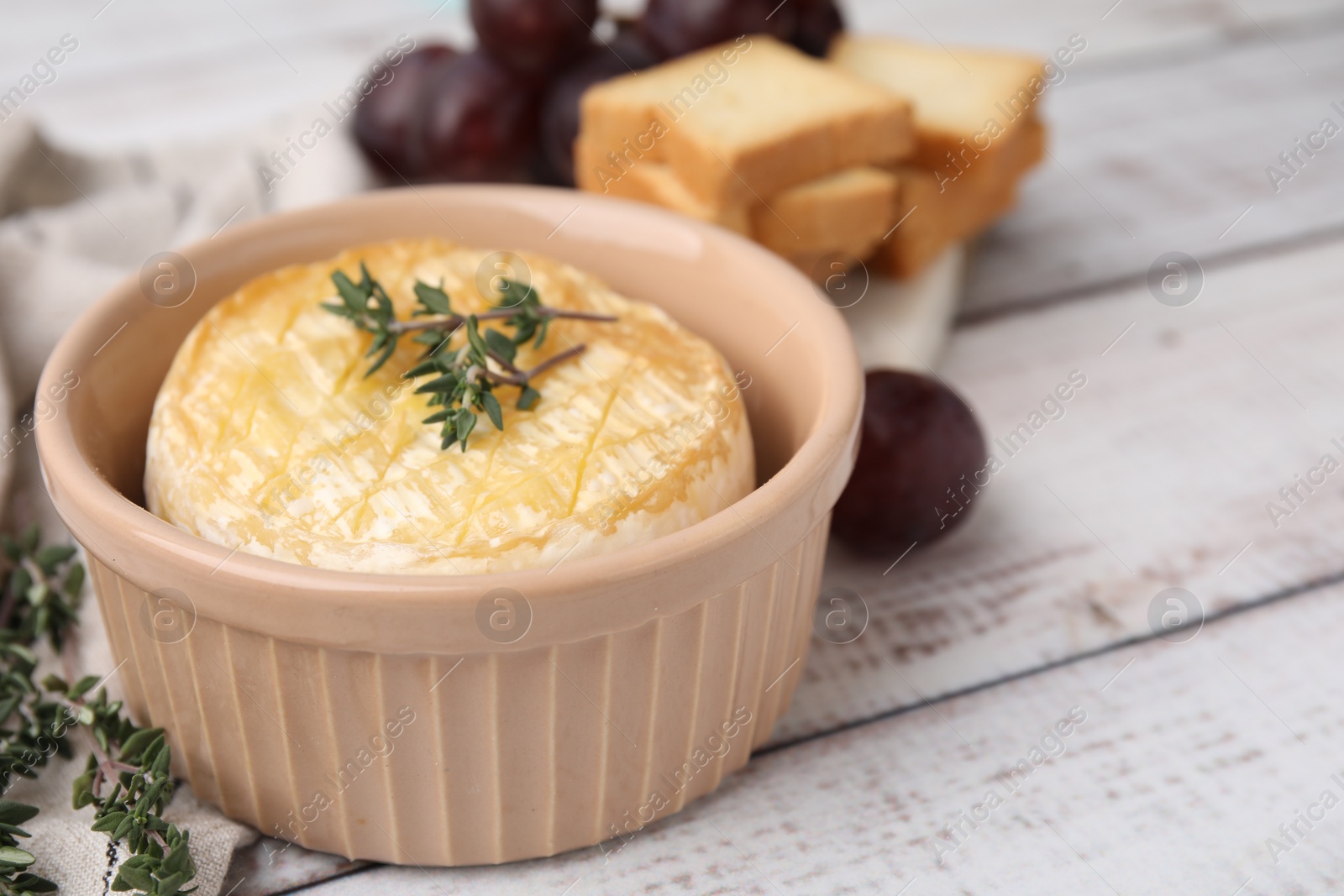 Photo of Tasty baked camembert and thyme in bowl on wooden table, closeup
