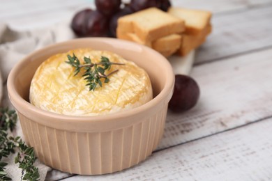 Tasty baked camembert and thyme in bowl on wooden table, closeup