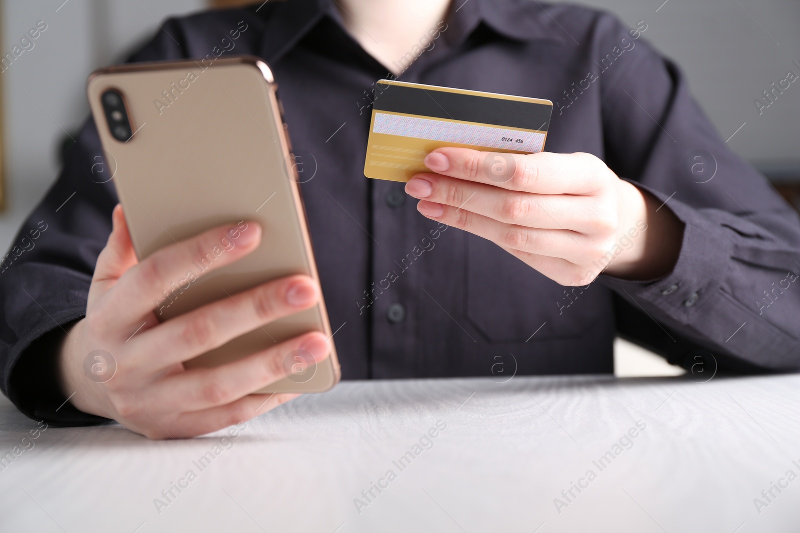 Photo of Online payment. Woman with smartphone and credit card at white wooden table, closeup