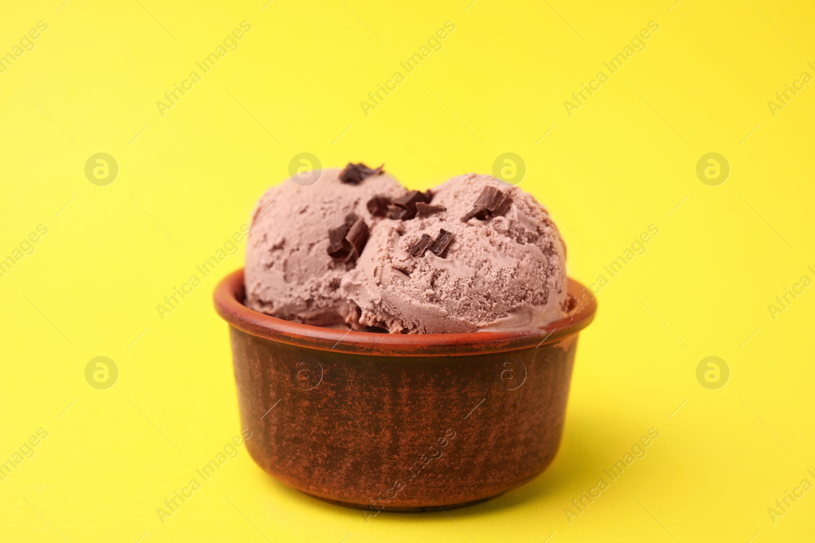 Photo of Bowl of tasty ice cream with chocolate chunks on yellow background, closeup