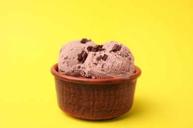 Photo of Bowl of tasty ice cream with chocolate chunks on yellow background, closeup