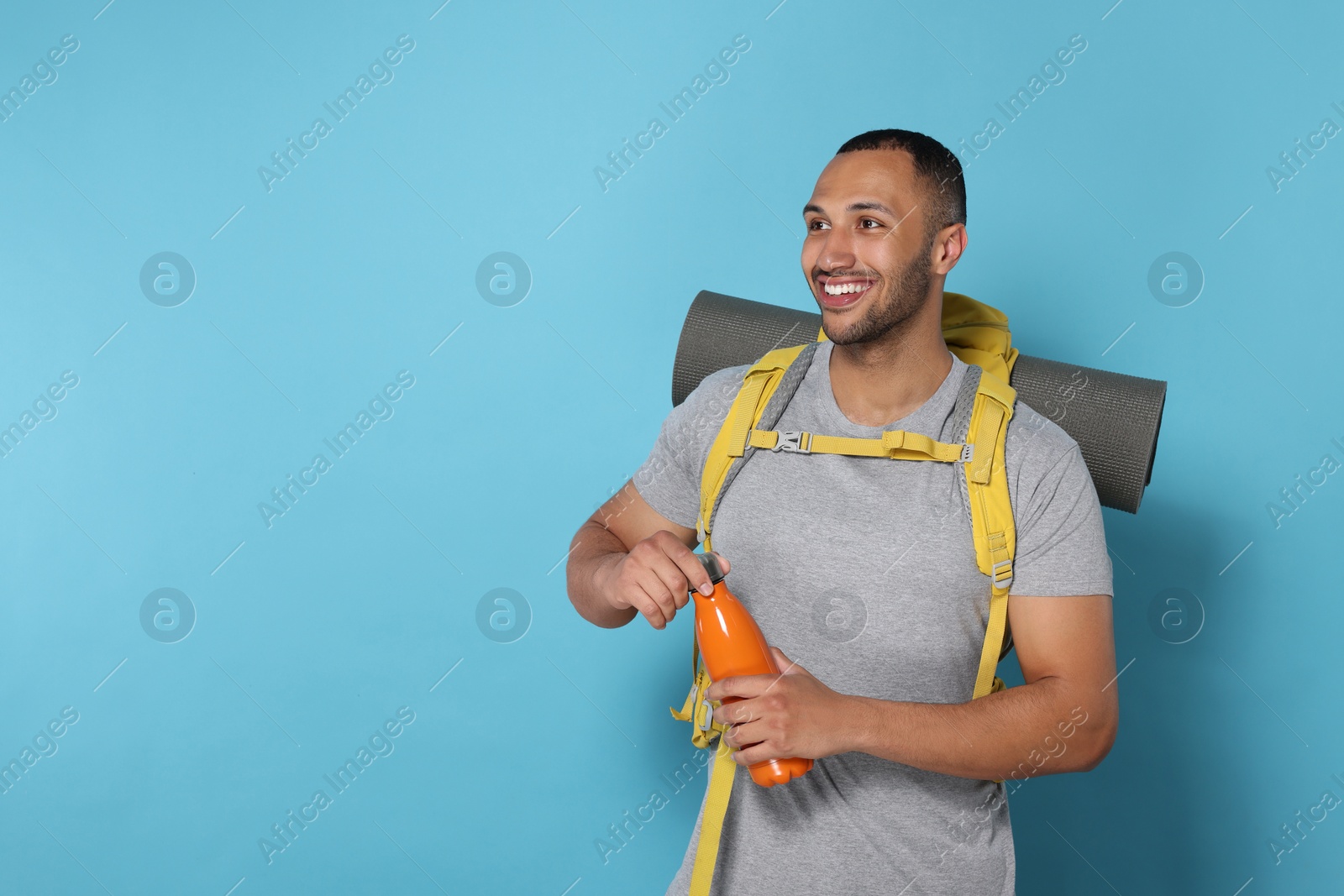 Photo of Happy tourist with backpack and thermo bottle on light blue background, space for text