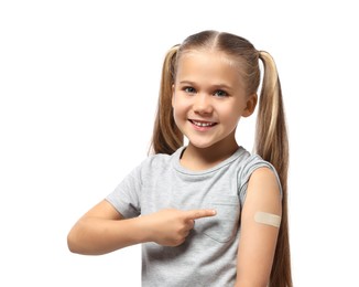 Photo of Happy girl pointing at sticking plaster after vaccination on her arm against white background