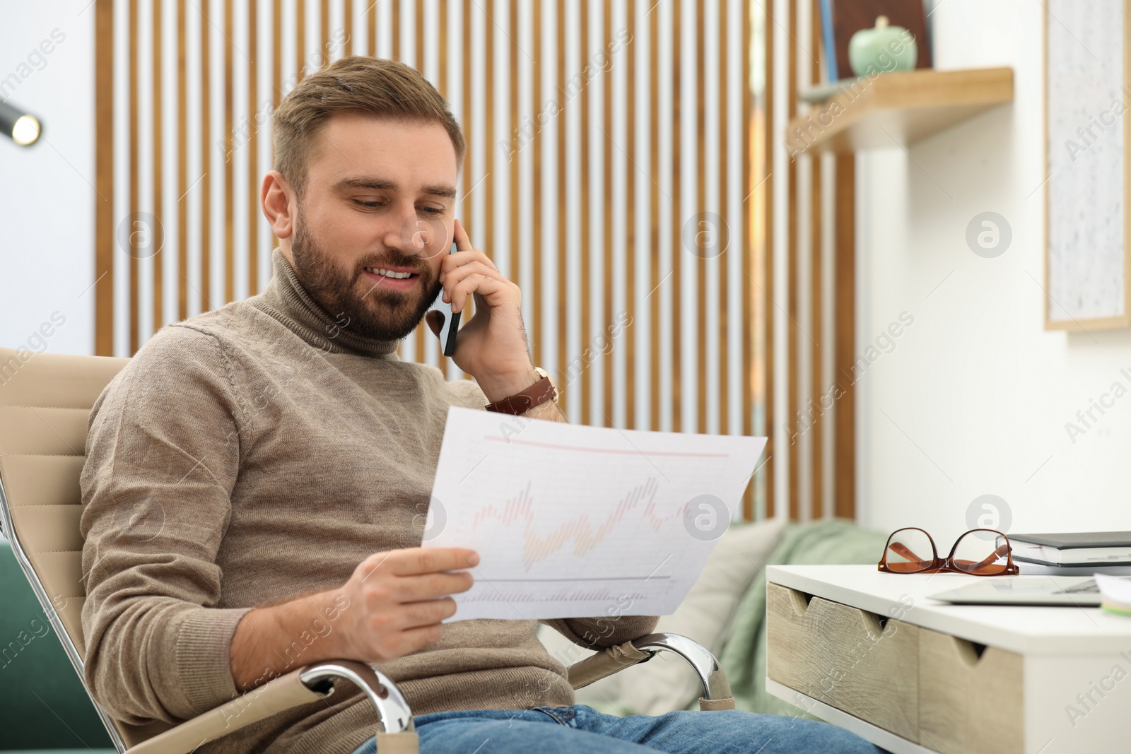 Photo of Young man talking on phone while working at home