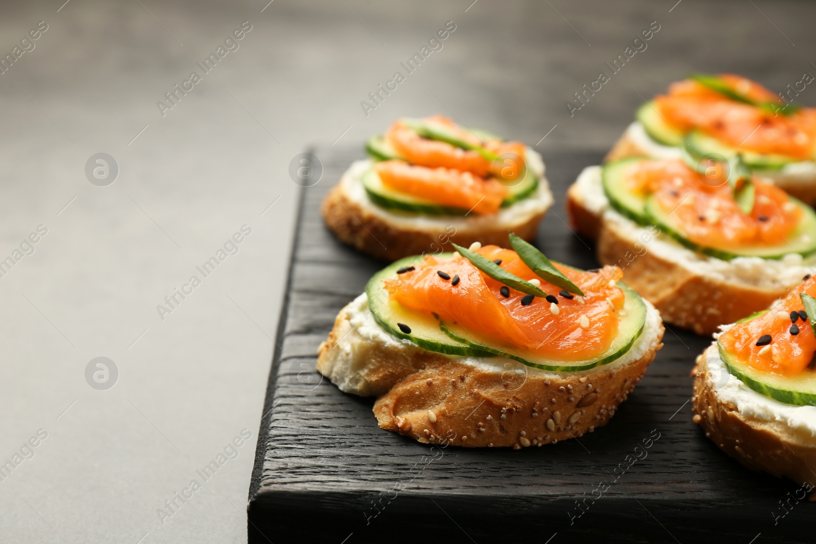 Photo of Tasty canapes with salmon, cucumber and cream cheese on grey table, closeup. Space for text