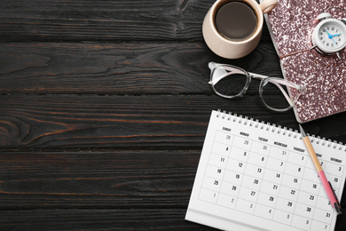 Photo of Flat lay composition with calendar and cup of coffee on black wooden table. Space for text