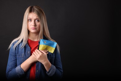 Photo of Sad woman holding Ukrainian flag on black background. Space for text