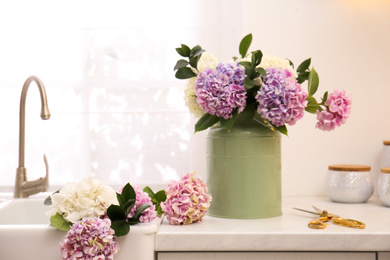 Photo of Bouquet with beautiful hydrangea flowers in can and scissors on light countertop