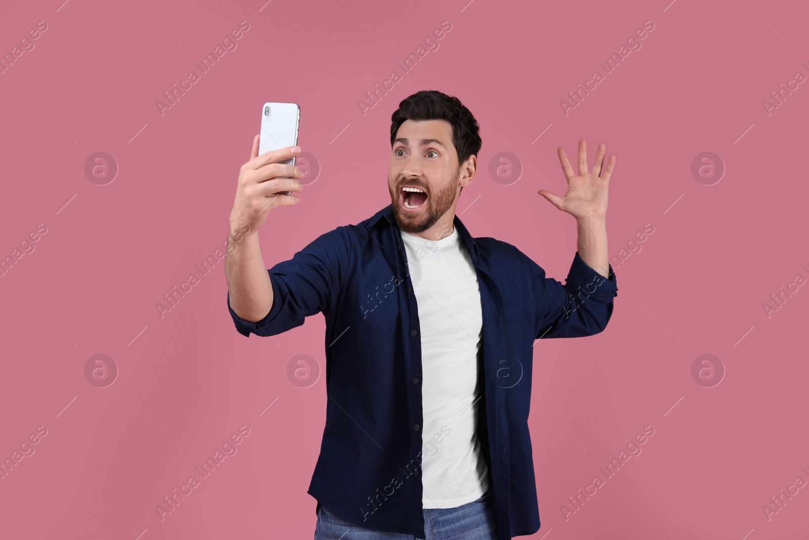 Photo of Surprised man taking selfie with smartphone on pink background