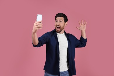 Photo of Surprised man taking selfie with smartphone on pink background