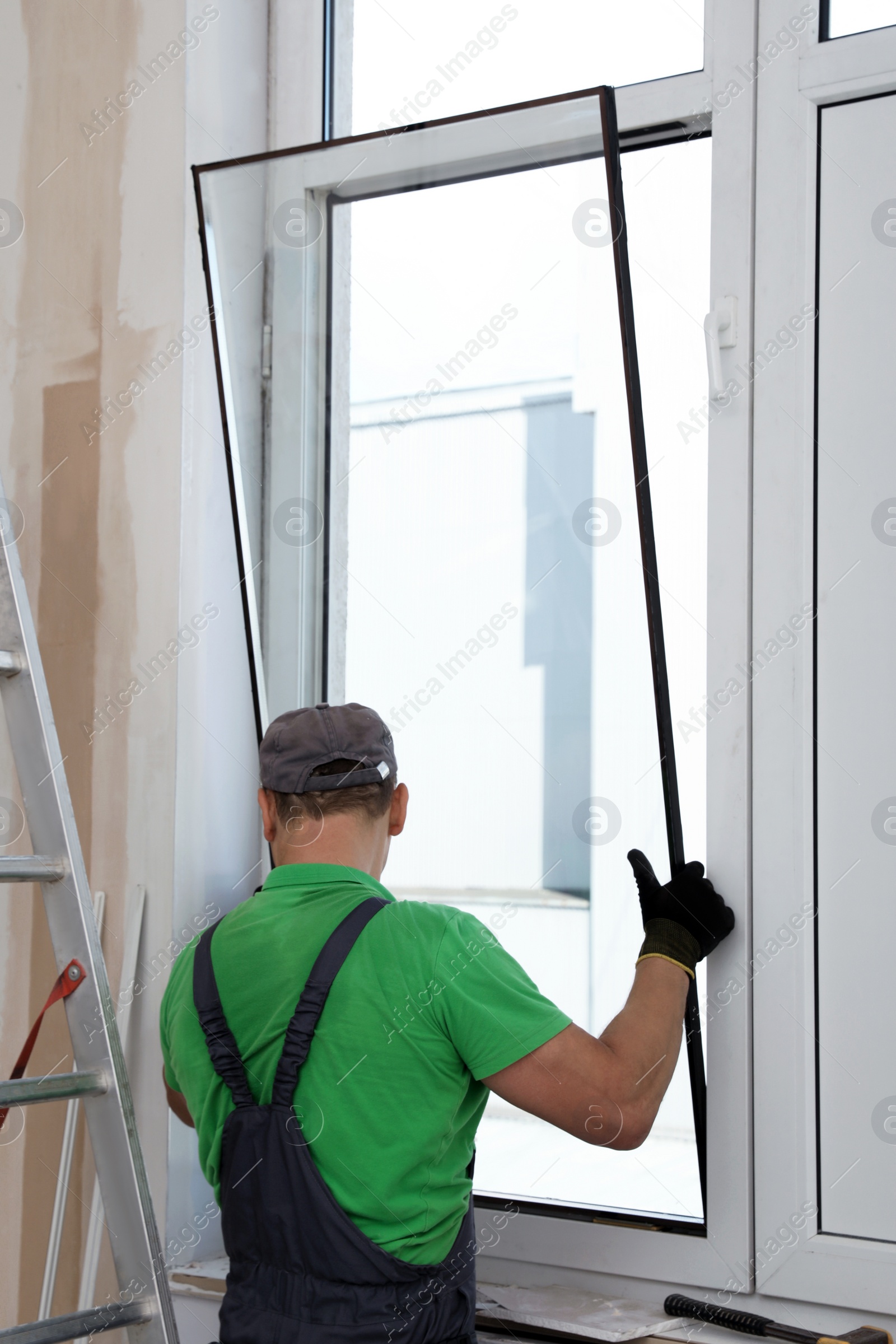 Photo of Worker in uniform installing double glazing window indoors, back view