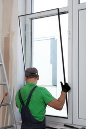 Worker in uniform installing double glazing window indoors, back view