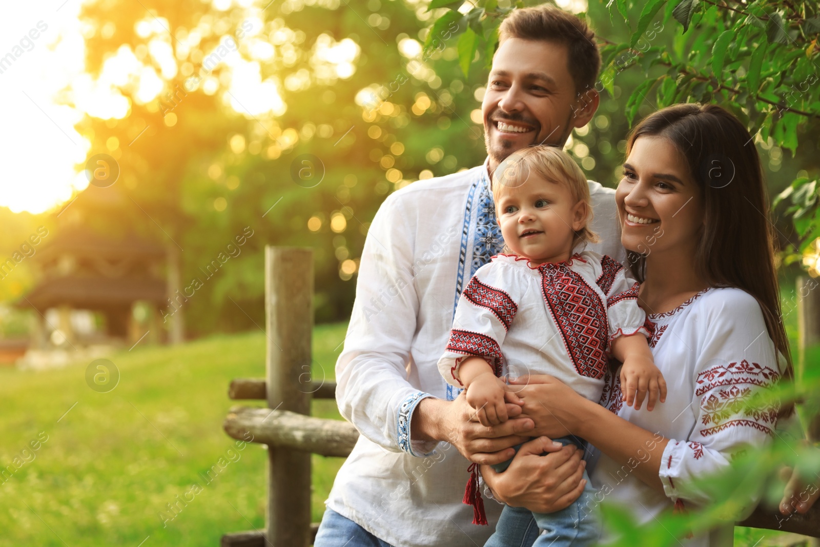 Photo of Happy cute family in embroidered Ukrainian shirts near rustic fence on sunny day. Space for text