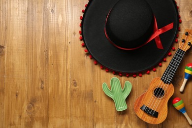 Photo of Mexican sombrero hat, maracas, toy cactus and guitar on wooden background, flat lay. Space for text