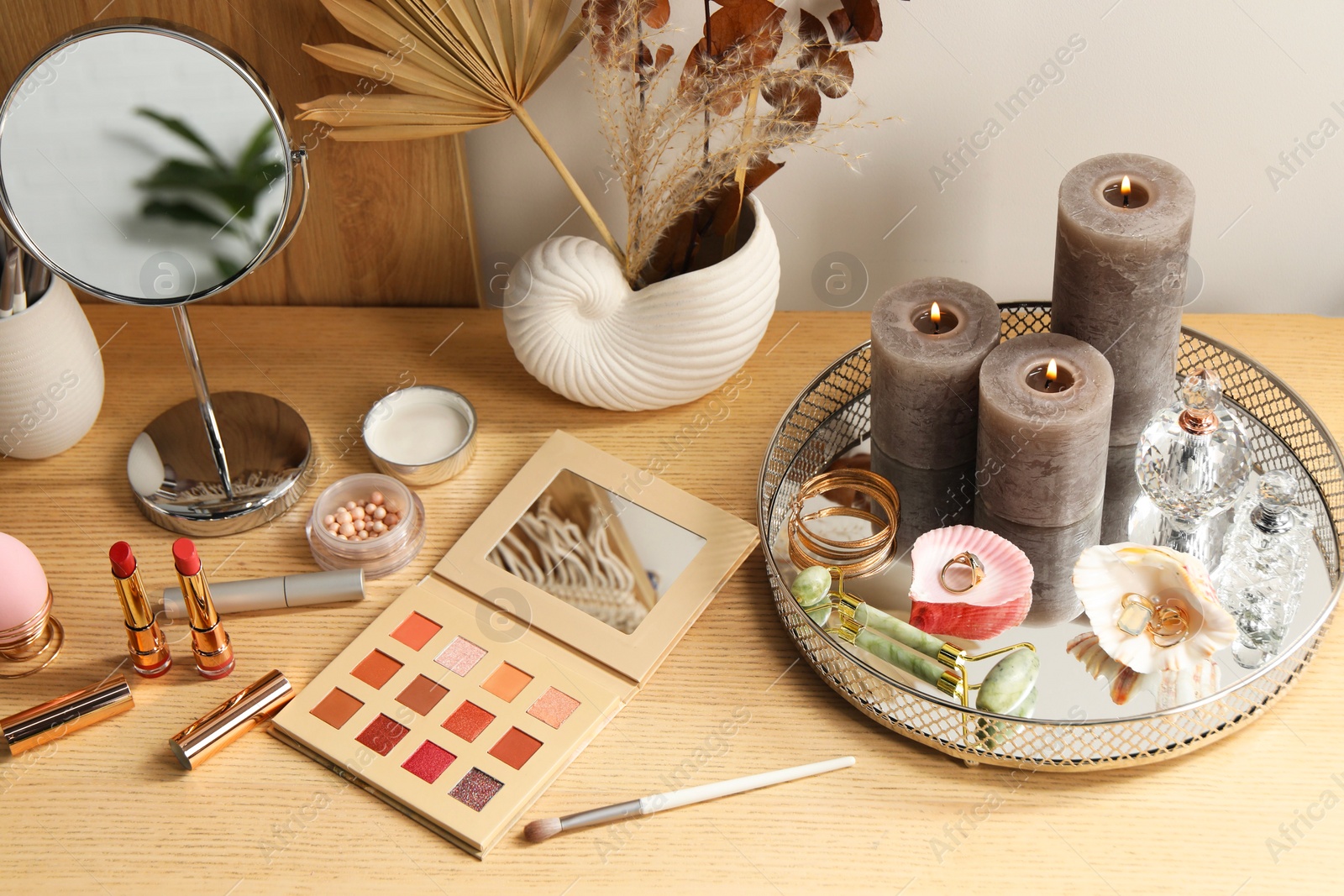 Photo of Perfumes, burning candles, jewelry and makeup products on wooden dressing table