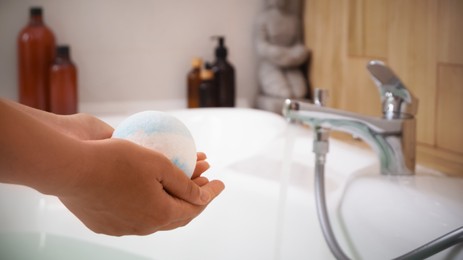 Woman holding bath bomb above tub indoors, closeup. Space for text