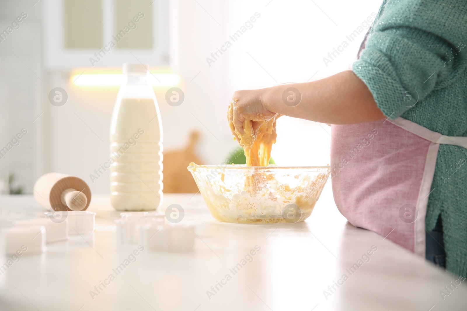 Photo of Little girl making dough at table in kitchen, closeup