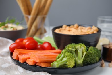 Plate with delicious hummus and fresh vegetables on white table, closeup