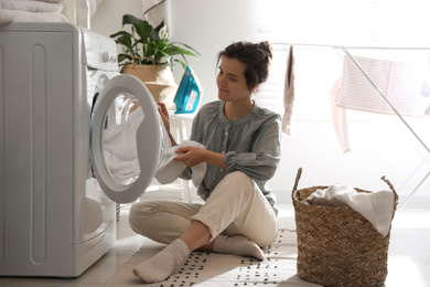 Photo of Young woman taking laundry out of washing machine at home