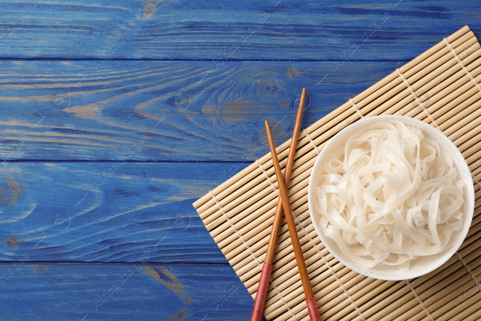 Photo of Bowl with rice noodles on wooden background, top view. Space for text