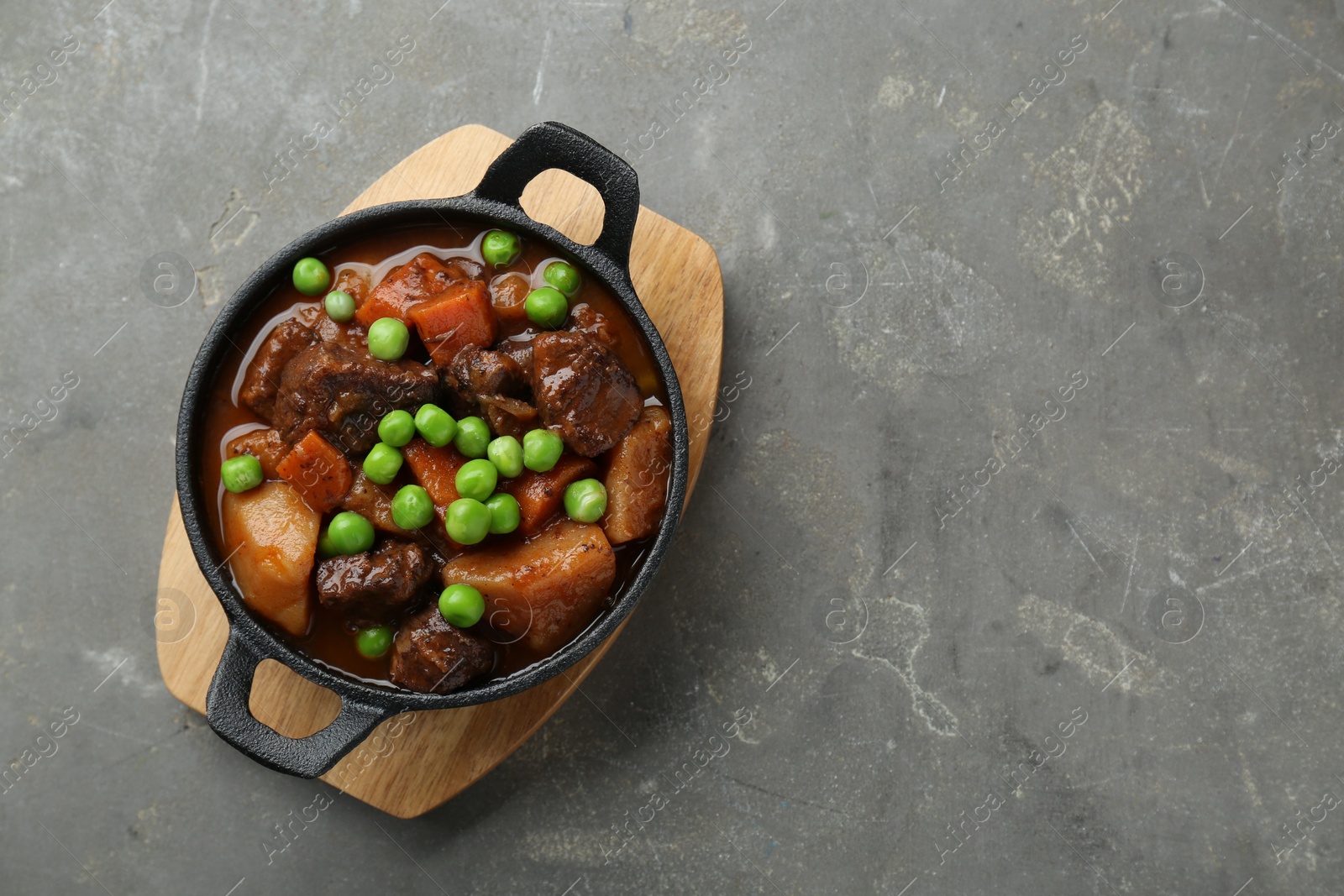 Photo of Delicious beef stew with carrots, peas and potatoes on grey table, top view. Space for text