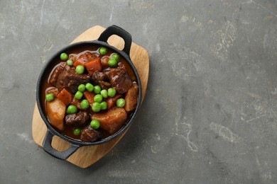 Delicious beef stew with carrots, peas and potatoes on grey table, top view. Space for text