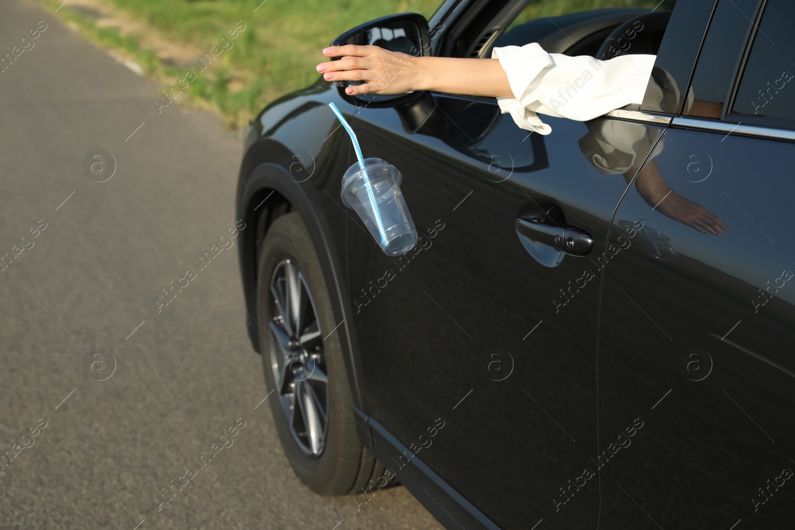 Photo of Driver throwing away plastic cup from car window. Garbage on road