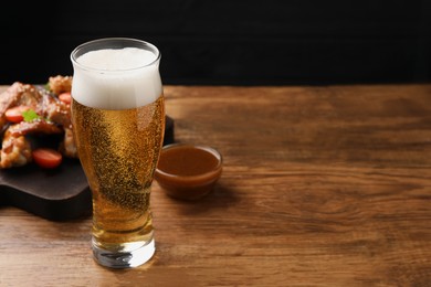 Glass of beer, delicious baked chicken wings and sauce on wooden table. Space for text