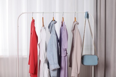 Photo of Clothing rack with stylish women's clothes on wooden hangers indoors