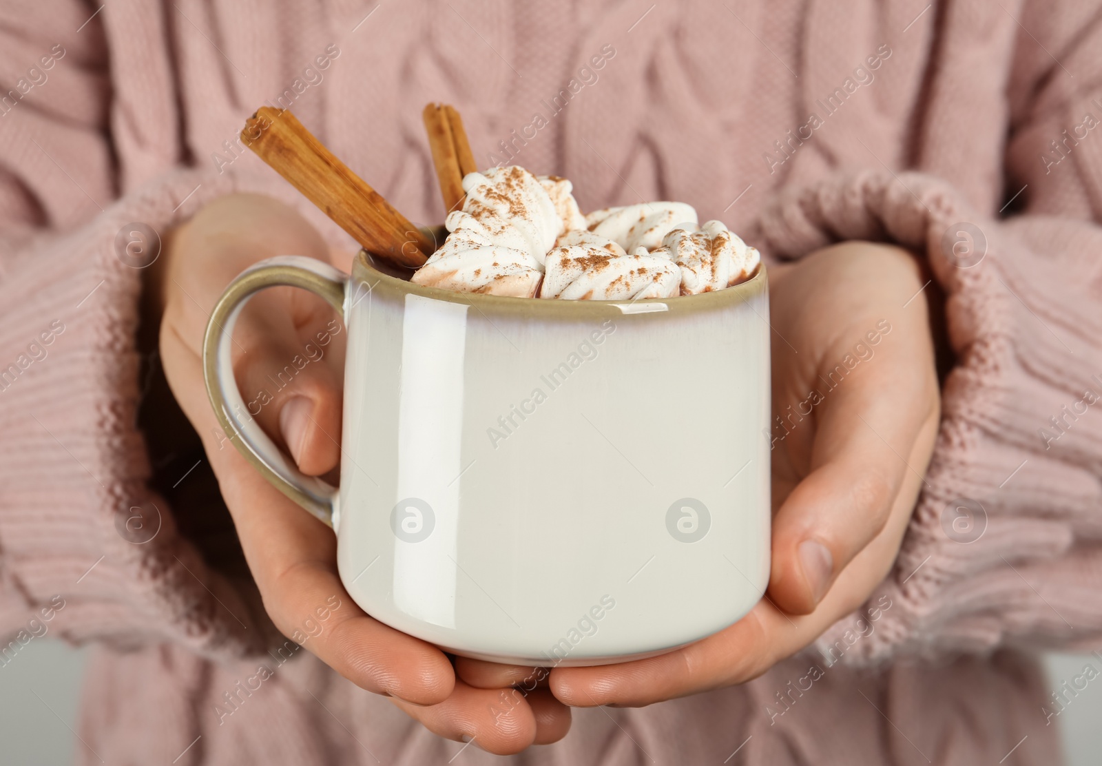 Photo of Woman holding cup of delicious hot chocolate with marshmallows and cinnamon sticks, closeup