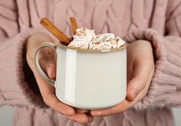 Woman holding cup of delicious hot chocolate with marshmallows and cinnamon sticks, closeup