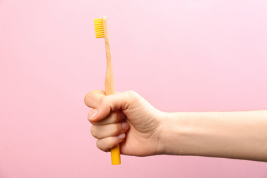 Woman holding bamboo toothbrush on pink background, closeup