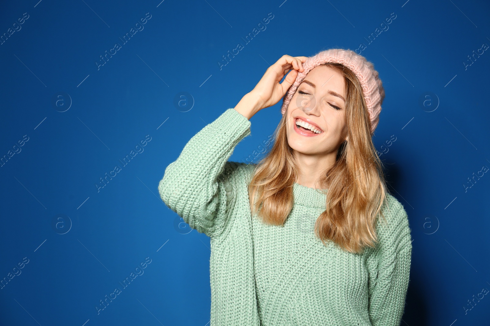 Image of Happy young woman wearing warm sweater and knitted hat on blue background 