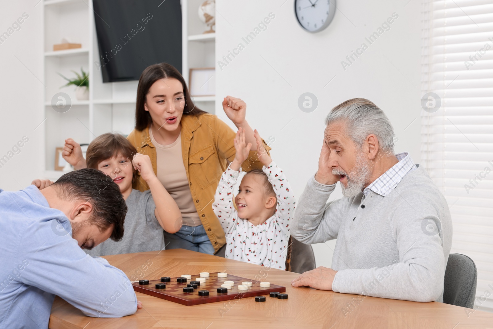 Photo of Emotional family playing checkers at wooden table in room