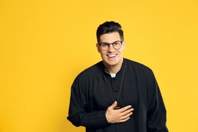Photo of Priest in cassock with clerical collar laughing on yellow background