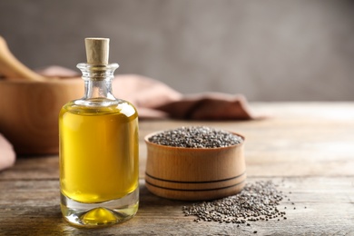 Photo of Bottle of chia oil and bowl with seeds on table. Space for text